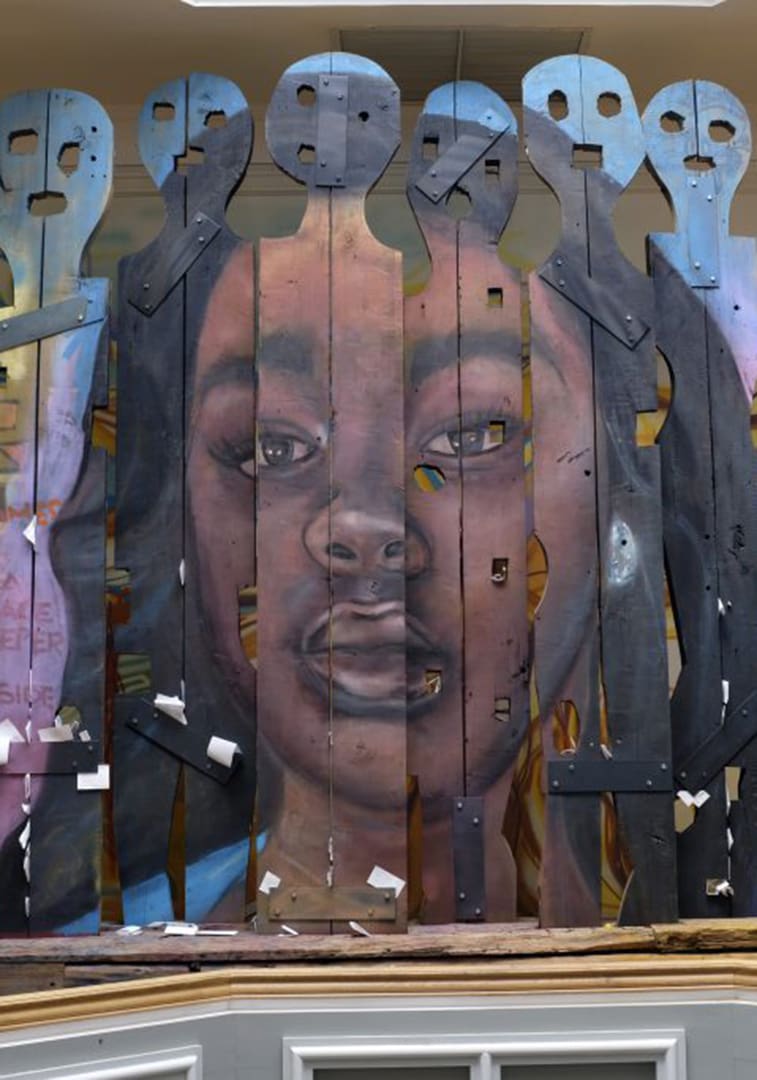 Wooden slats form a barrier, revealing a realistic portrait of a young girl's face through the gaps.