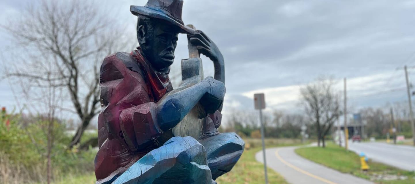 Colorful metallic statue of a jockey riding a horse outside a brick building.