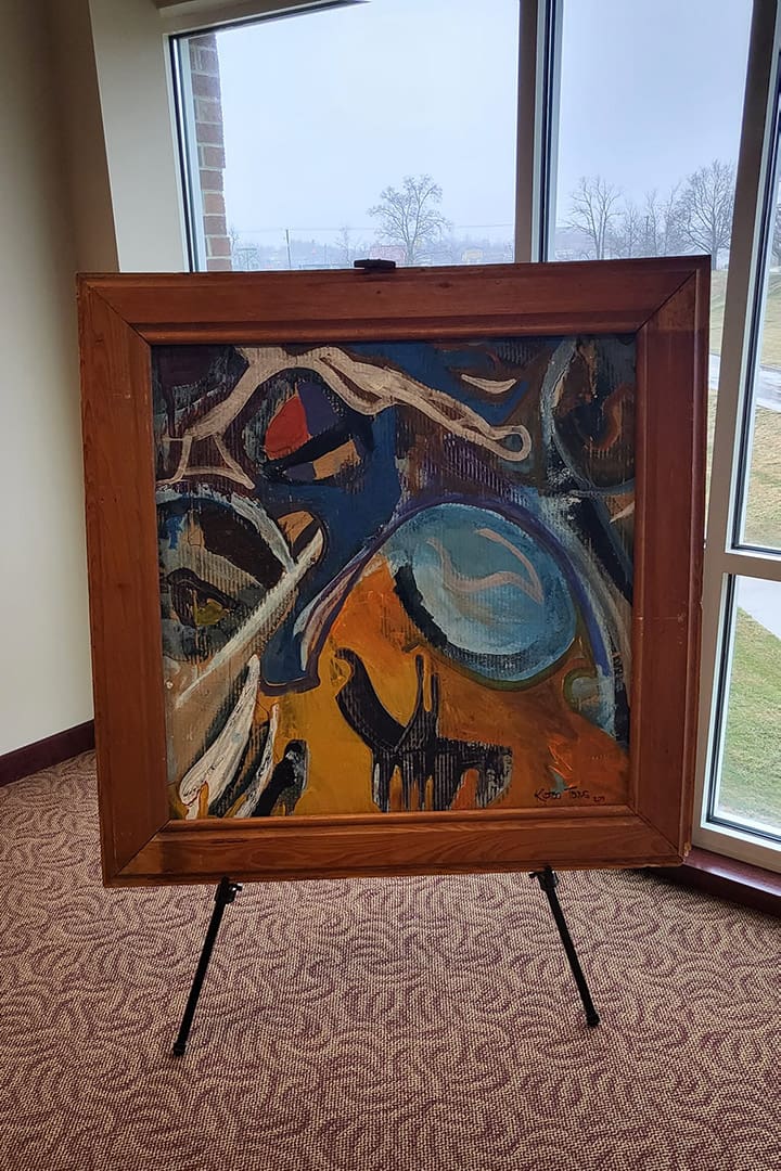 Abstract colorful painting on a wooden frame displayed on a black metal easel in a bright room by a windowed wall