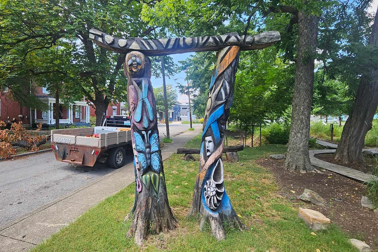 Colorfully painted wooden arch formed by two carved tree trunks in a park setting, featuring butterfly designs.